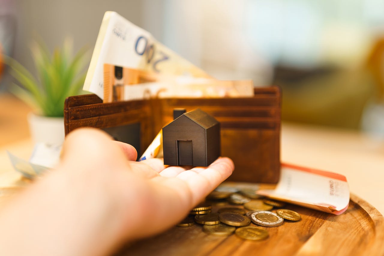 Crafting Captivating Headlines: Your awesome post title goes here A hand holding a small house model with euro notes and coins nearby, illustrating real estate investment and finance.