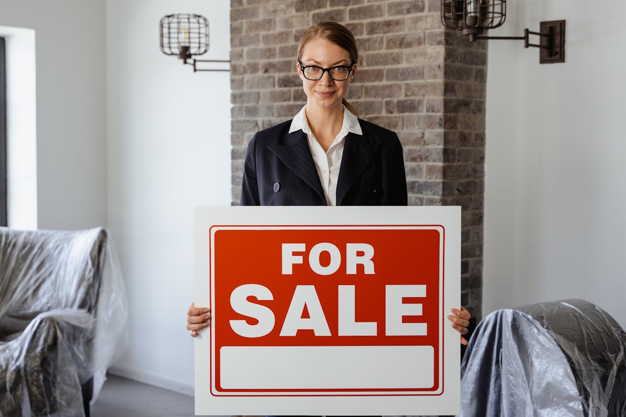 Professional real estate agent holding a 'For Sale' sign inside a modern interior.